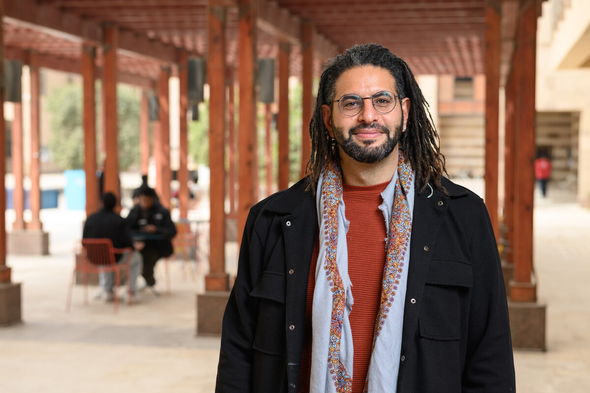 A man stands in front of a wooden gazebo at AUC New Cairo